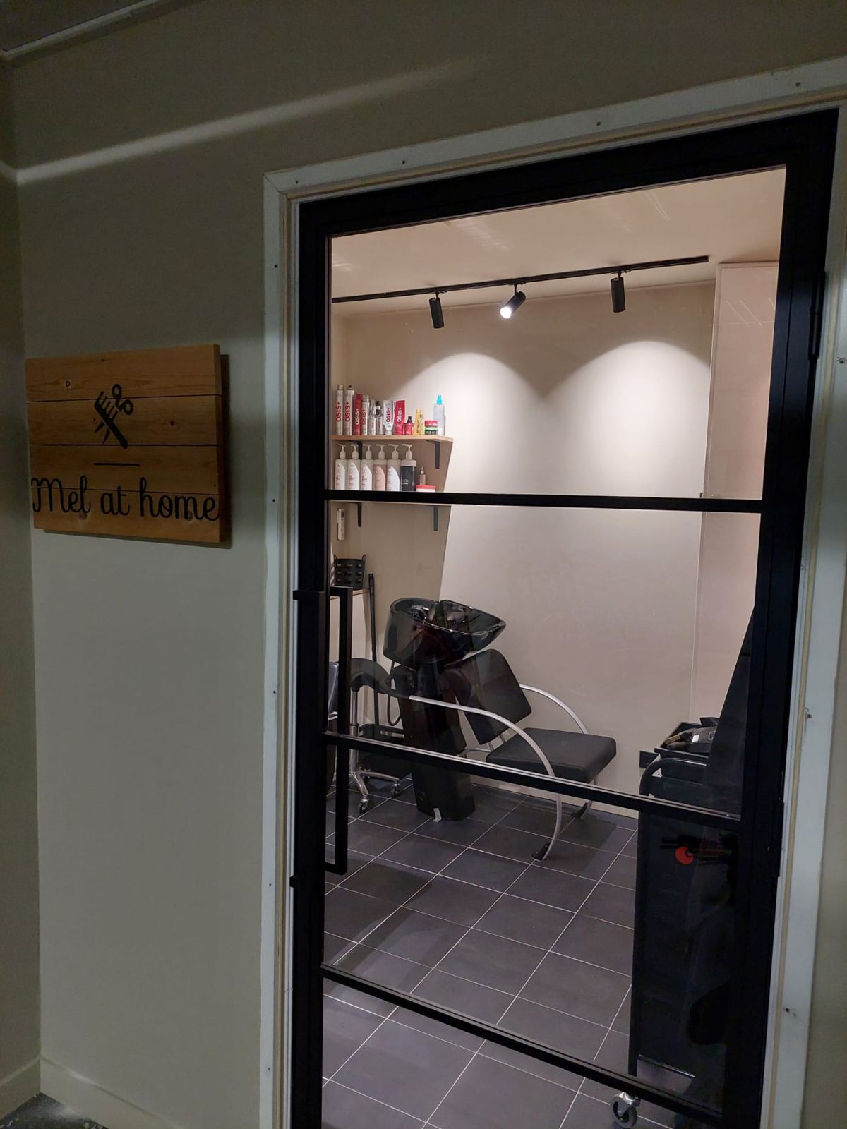 Door de stalen glazen deur kijk je de salon in, met het houten naambord ernaast
